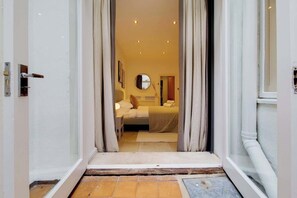 A hotel room with a bed, a bedside table, a mirror, and a door leading to the outside. - CWG1 - Elegant 3-Bed on Kensington Garden Square (London)