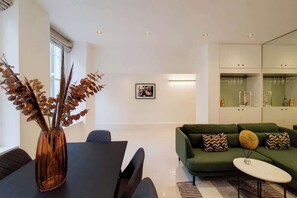 A modern living room with a green sofa, a dining table, and a vase with dried plants. - CWG1 - Elegant 3-Bed on Kensington Garden Square (London)