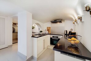 A modern kitchen with white cabinetry, a black countertop, and a bowl of fruit. - CWG1 - Elegant 3-Bed on Kensington Garden Square (London)