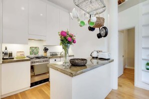 Une cuisine moderne avec des meubles blancs, une cuisinière à gaz, un évier et un porte-ustensiles suspendu.