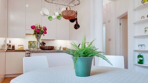 A modern kitchen with white cabinets, a dining table with a polka dot tablecloth, a potted fern, and hanging kitchen utensils. - VY6 - Stylish Loft-Style 1-Bed Near Borough Market (Greater London)