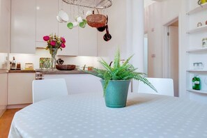 Eine moderne Küche mit weißen Schränken, einem Esstisch mit puntiertem Tischläufer, einem Topfhanf und hängenden Küchenutensilien.