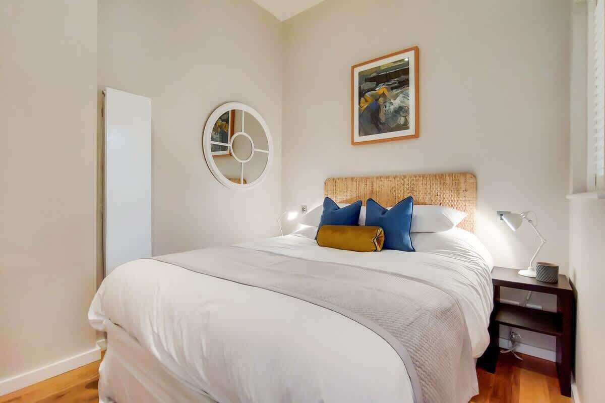 Una camera da letto con un letto, una sveglia a muro rotonda, un quadro incorniciato, un comodino con una lampada e un altro comodino.