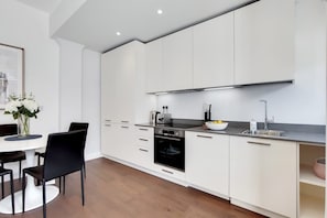 Une cuisine moderne avec des meubles blancs, un plan de travail noir et un coin repas comprenant une table blanche et des chaises noires.