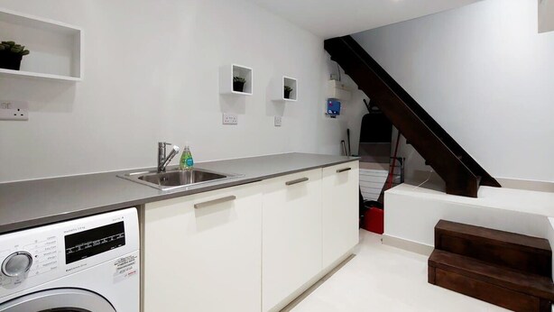 Una cocina moderna con lavadora integrada, un lavamanos y una escalera que sube a otro nivel.