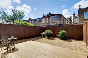 Ein Garten mit einer Holterrasse, einem kleinen Tisch und zwei Kübelpflanzen.