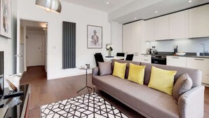 Una sala de estar moderna con un sofá, una mesa de centro, una lámpara colgante y una cocina al fondo.
