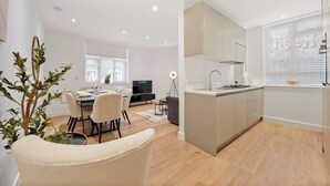 Et moderne køkken med en central ø, et spiseområde med stole, og et fjernsyn i baggrunden.