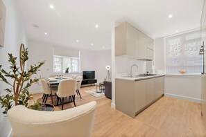 Eine moderne Küche mit einer zentralen Kochinsel, einem Essbereich mit Stühlen und einem Fernseher im Hintergrund.