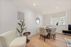 Un comedor moderno con una mesa redonda, sillas, una mesita auxiliar, una planta en maceta y un espejo en la pared.