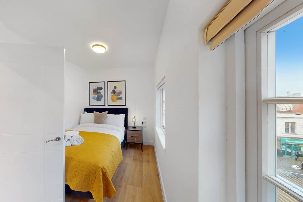 A narrow hotel room with a bed, a bedside table, a nightstand, a window, and a door.