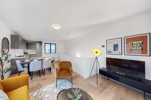Ein modernes Wohnzimmer mit Fernseher, einem Essbereich und einer Küche im Hintergrund.