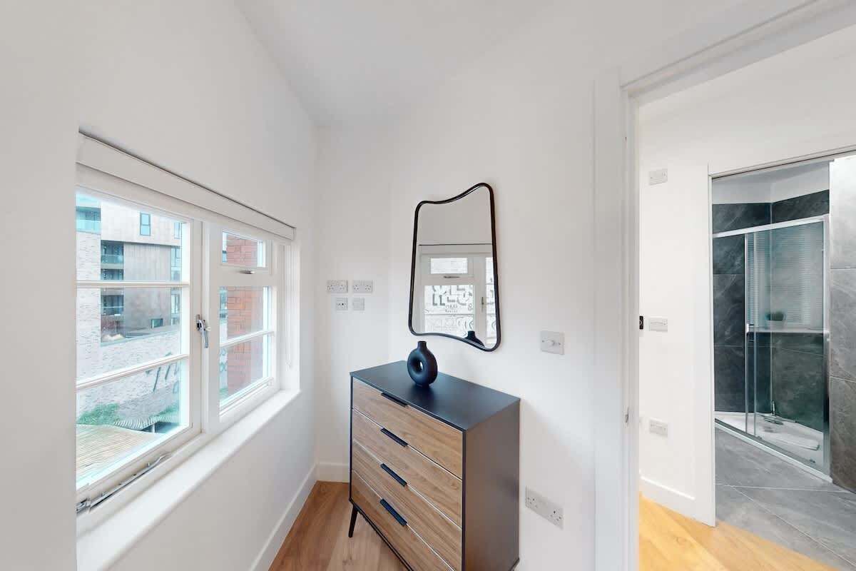 Una habitación con ventana, cómoda, espejo y zona de ducha.