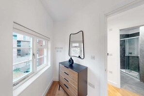 Ein Zimmer mit Fenster, einem Schminktisch, einem Spiegel und einer Dusche.