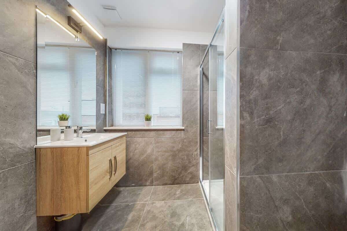 Une salle de bain moderne avec un meuble-lavabo en bois, un grand miroir et une cabine de douche en verre.