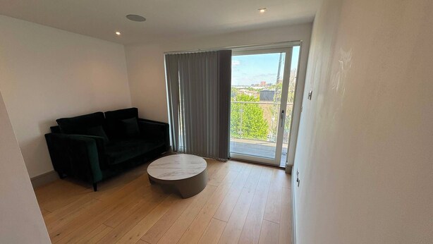 A modern living room with a black sofa, a round coffee table, and a sliding glass door leading to a balcony. - The Zenith Residence - 2 Bedroom (London)