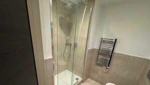 A modern bathroom with a glass-enclosed shower, a white toilet, and a chrome towel rack. - The Zenith Residence - 2 Bedroom (London)