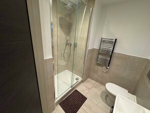 Ein modernes Badezimmer mit einer gläsernen Dusche, einer weißen Toilette und einem chromfarbenen Handtuchhalter.