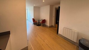 A room with a wooden floor, a round table with two chairs, a radiator, and a door leading to another room. - The Zenith Residence - 2 Bedroom (London)