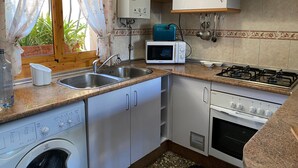 Eine kleine Küche mit Waschmaschine, Mikrowelle, Gaskochfeld und Spüle.