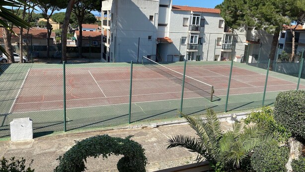 Ein Tennisplatz im Freien, umgeben von Wohngebäuden, Bäumen und einem klaren Himmel.