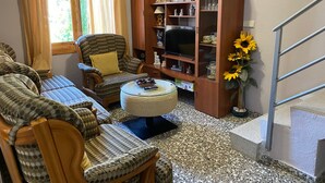 Ein Wohnzimmer mit einer Sofagarnitur, einem Fernseher, einem Bücherregal und einer Treppe.