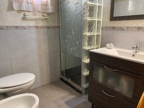 Et badeværelse med toilet, glasbrusekabine, vask og skab.