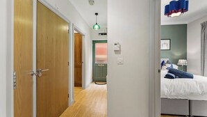 Et soveværelse med seng, natbord, lampe og et vindue med gardiner.