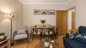 En hyggelig stue med spiseplads, en sofa, en lampe og en dør til et andet rum.