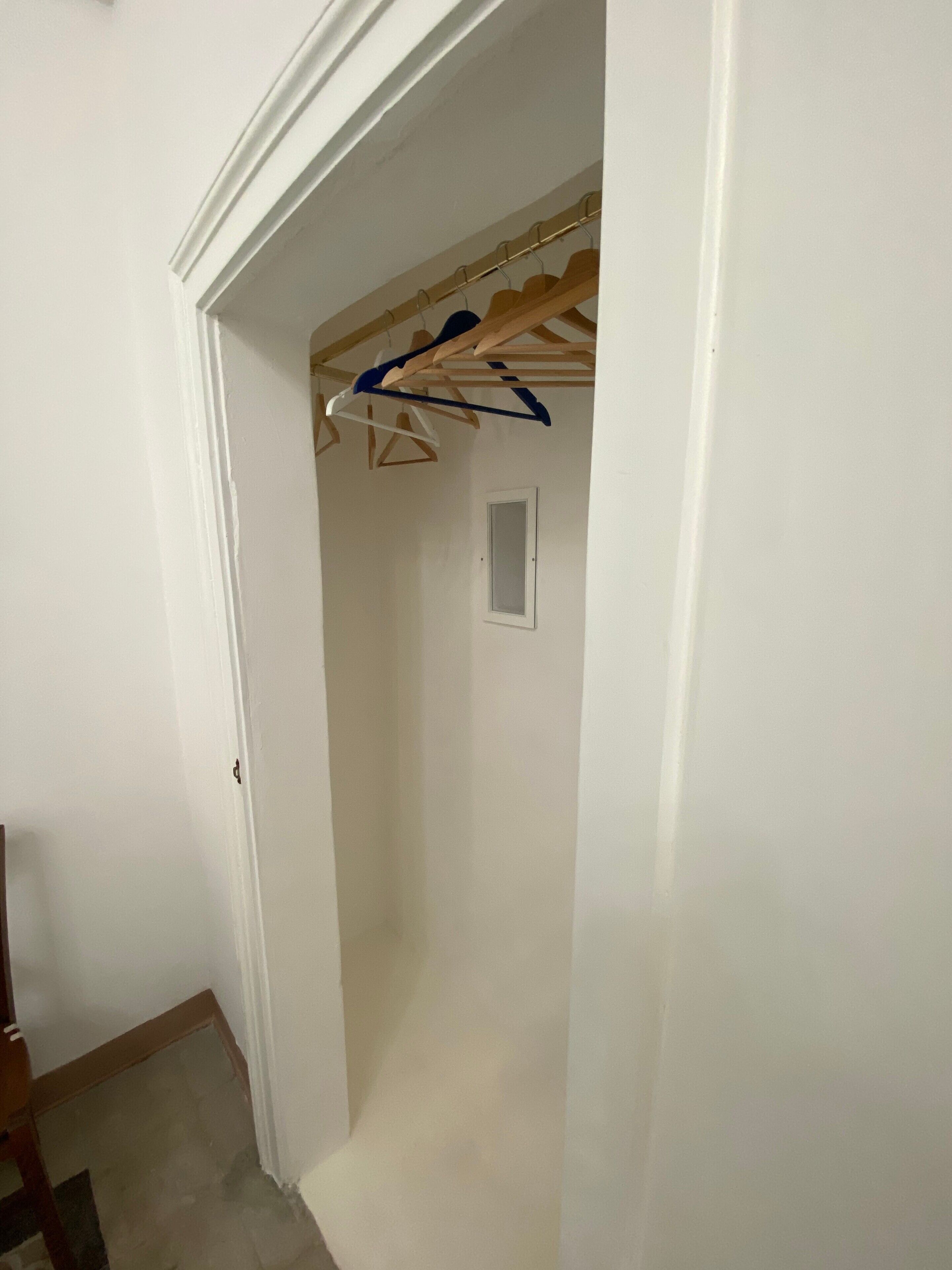 Ein schmaler Flur mit einer Holztürrahmung, einer weißen Wand und einem Kleiderständer mit Kleidung.