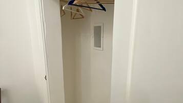 Ein schmaler Flur mit einer Holztürrahmung, einer weißen Wand und einem Kleiderständer mit Kleidung.
