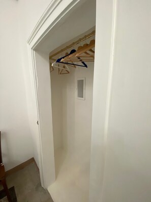 Un pasillo estrecho con un marco de puerta de madera, una pared blanca y un perchero con ropa.