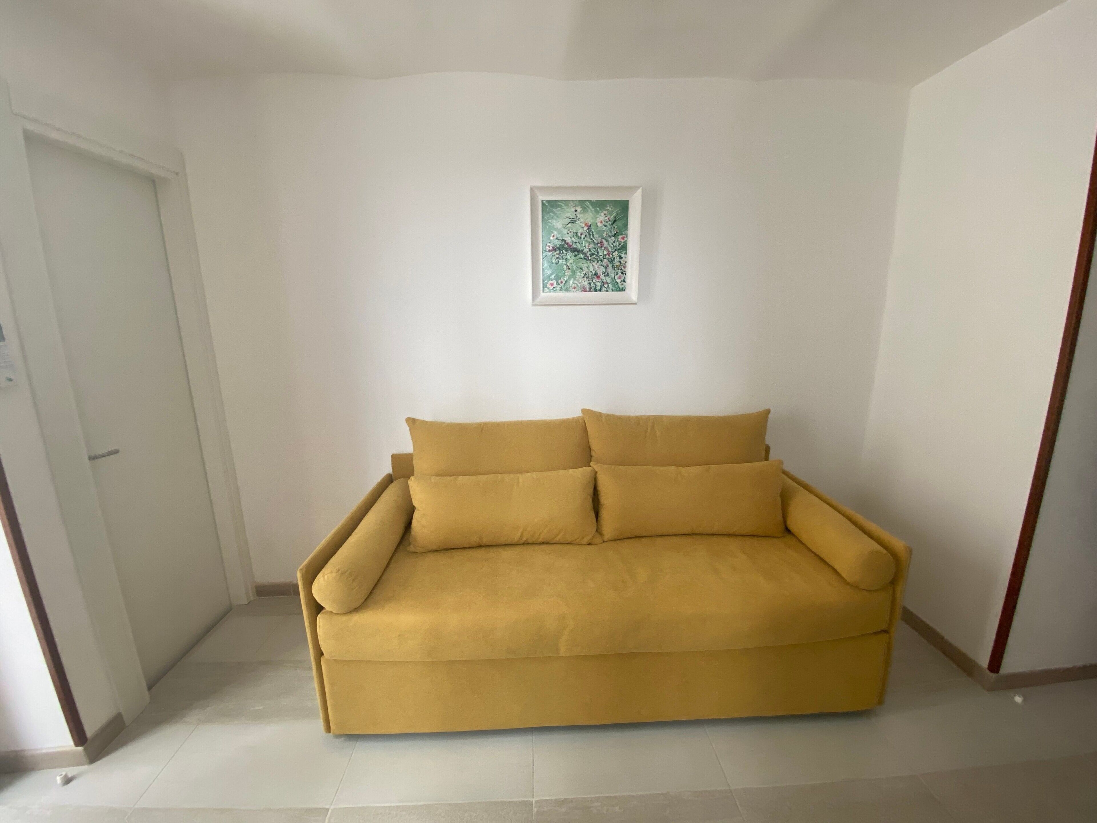 Una stanza con un divano giallo, una porta e un quadro incorniciato appeso al muro.