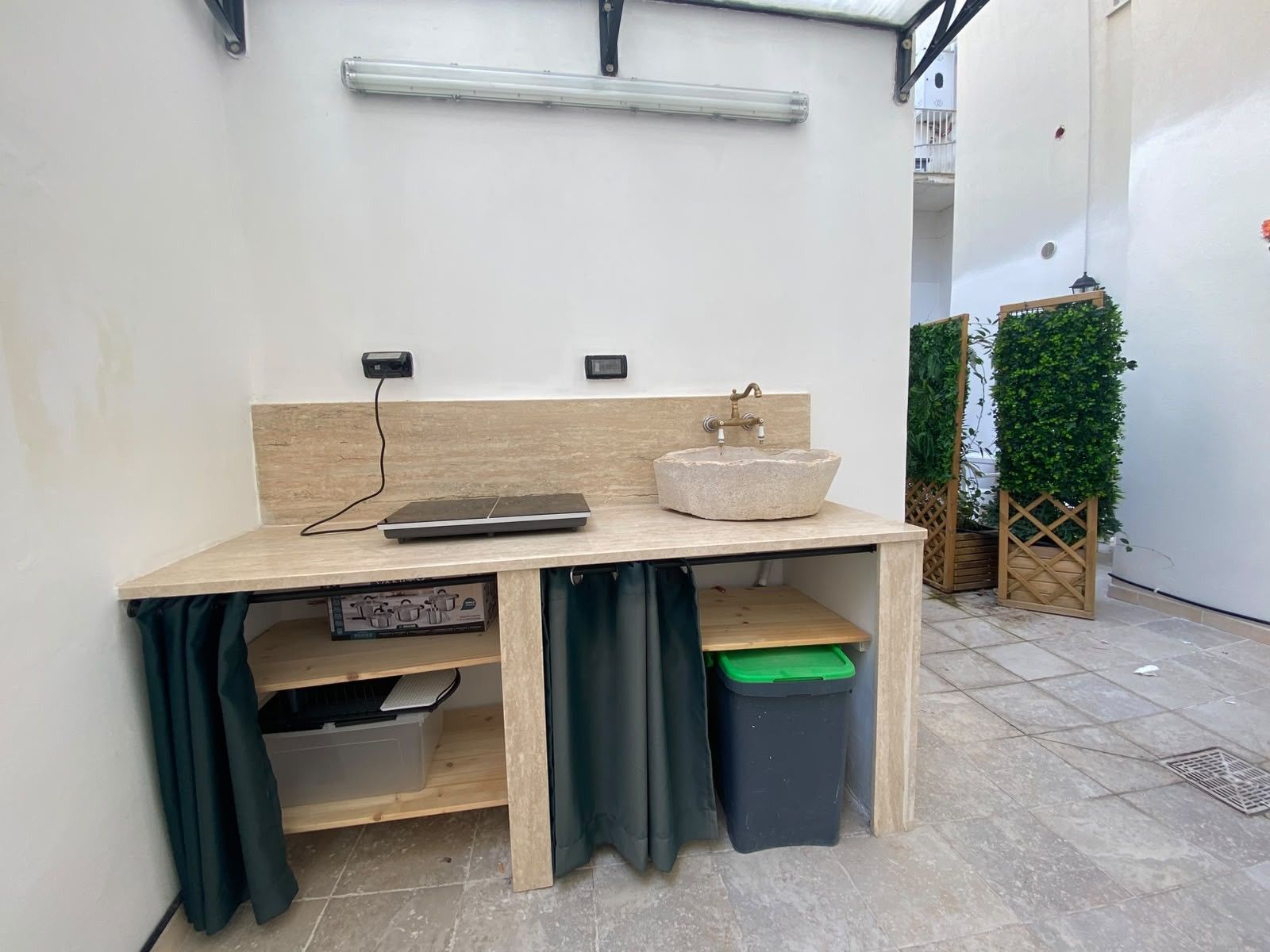 A small outdoor workspace with a wooden table, a sink, and a trash bin.