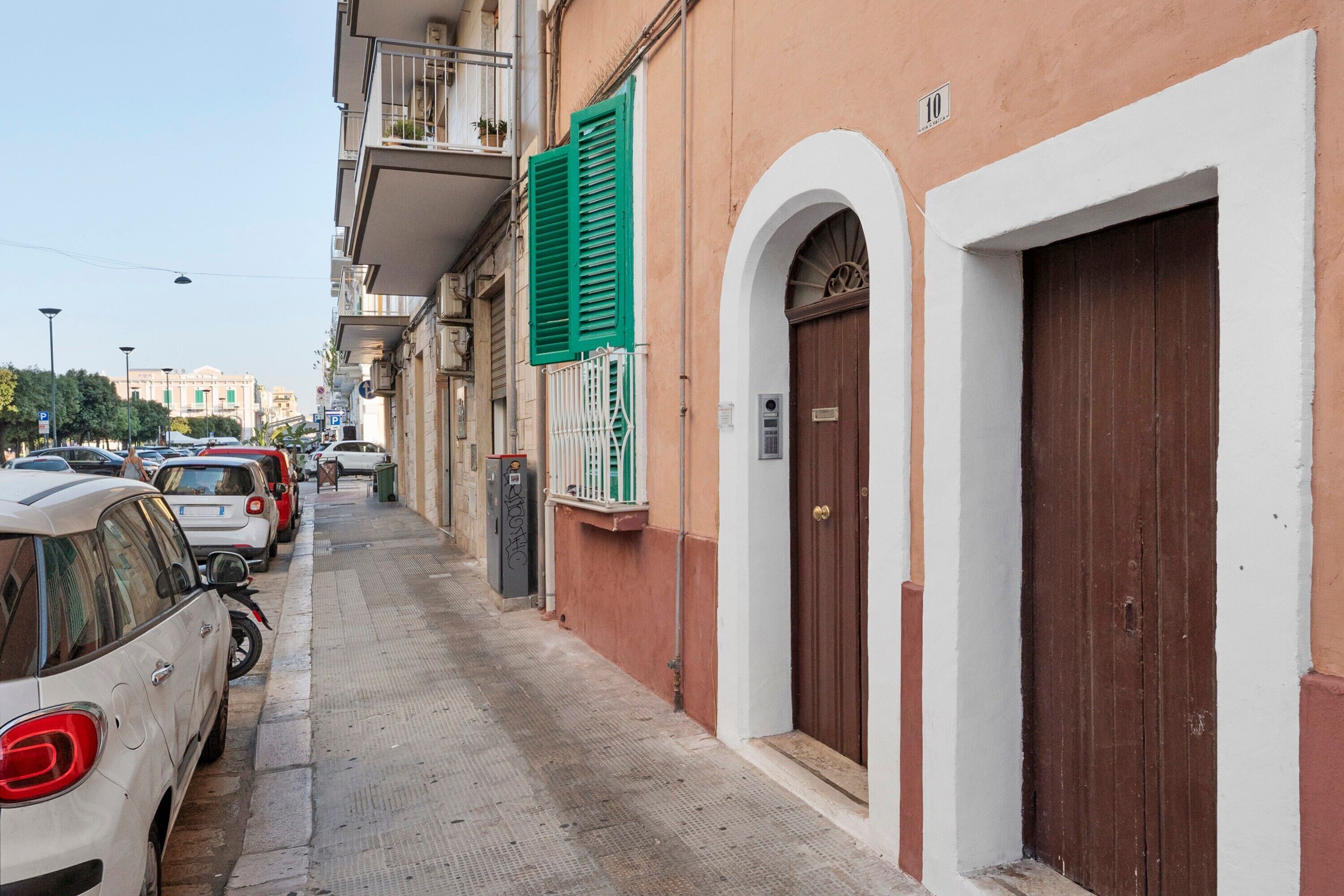 Une rue étroite, bordée de voitures garées, et un immeuble avec une porte marron et un volet vert.