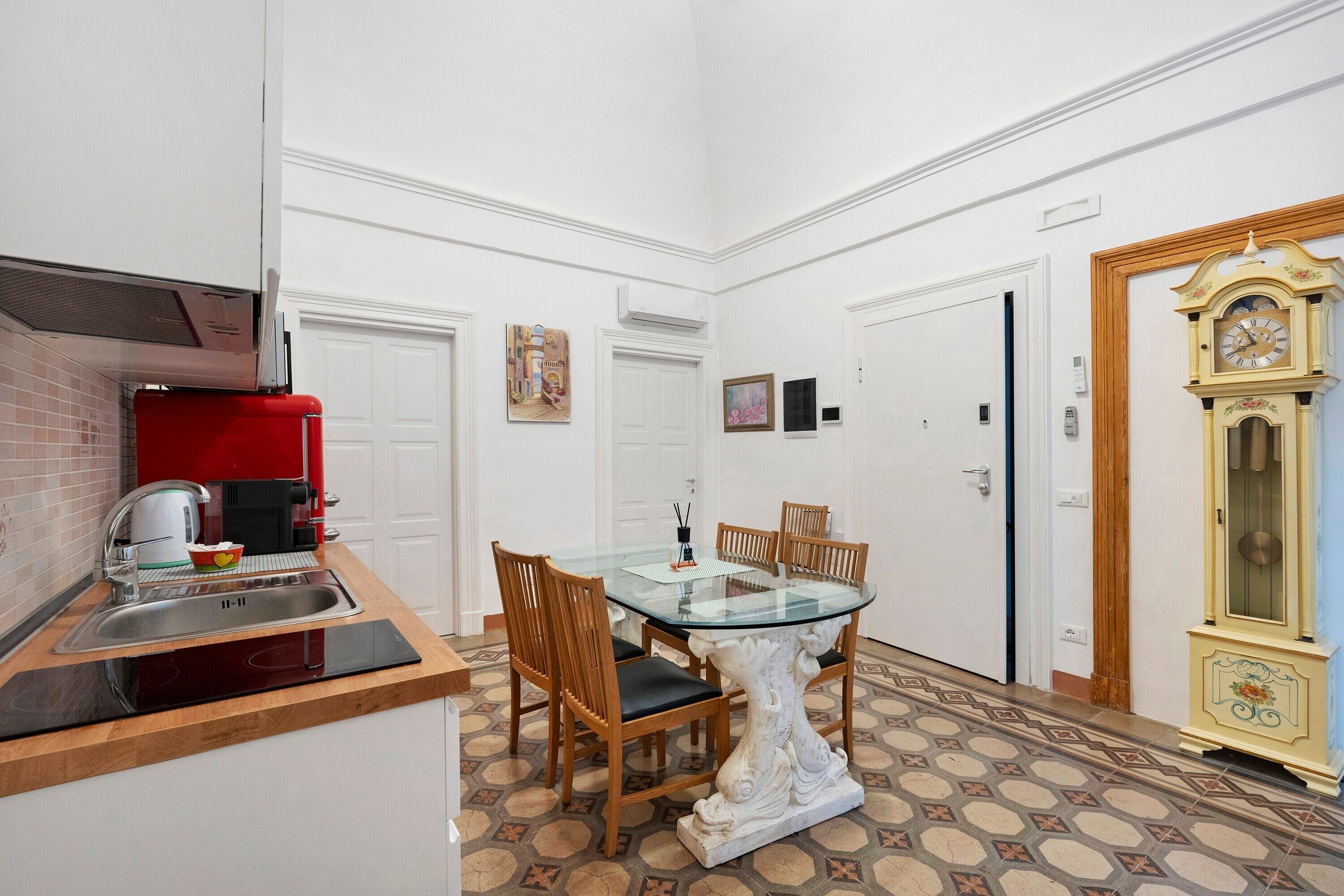 Une cuisine de taille réduite avec un appareil électroménager rouge, une table à manger avec des chaises et une horloge décorative.