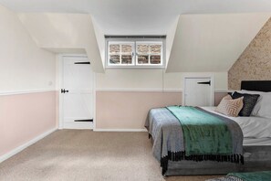 Une chambre avec un plafond en pente, une fenêtre avec des volets, un lit recouvert d’une couverture verte et une porte dotée d’une poignée noire.