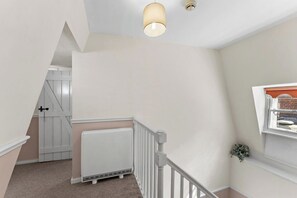 Un escalier avec une rampe blanche, un radiateur et une porte donnant sur une autre pièce.