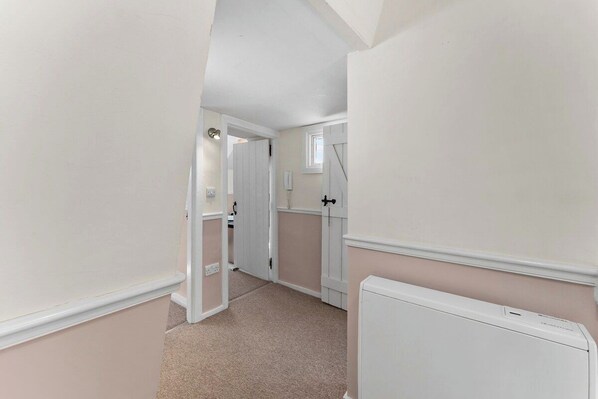 A narrow hallway with a radiator, a door leading to another room, and a light switch on the wall.