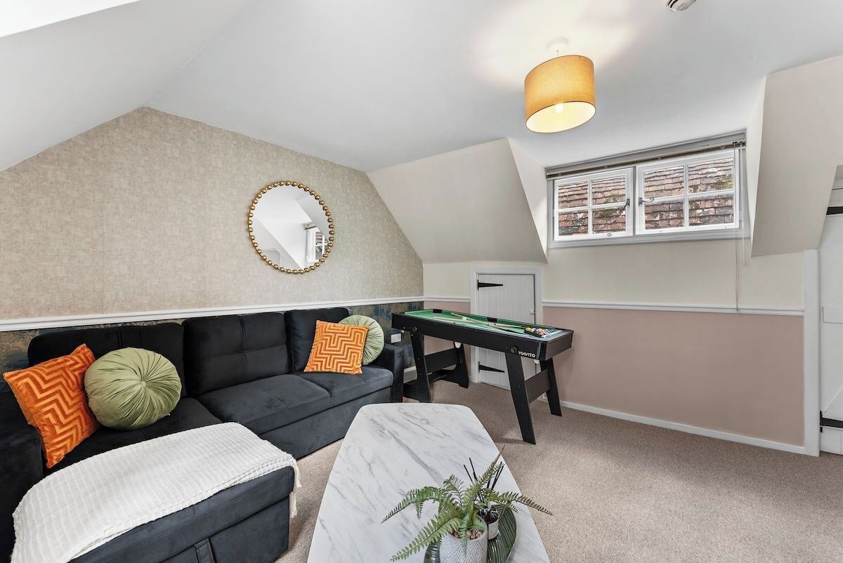 A cozy room with a black sofa, a white coffee table, a green plant, a billiards table, and a mirror on the wall.