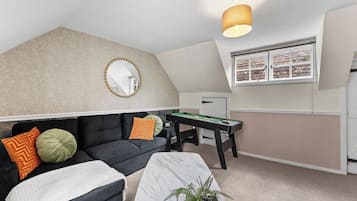 A cozy room with a black sofa, a white coffee table, a green plant, a billiards table, and a mirror on the wall.