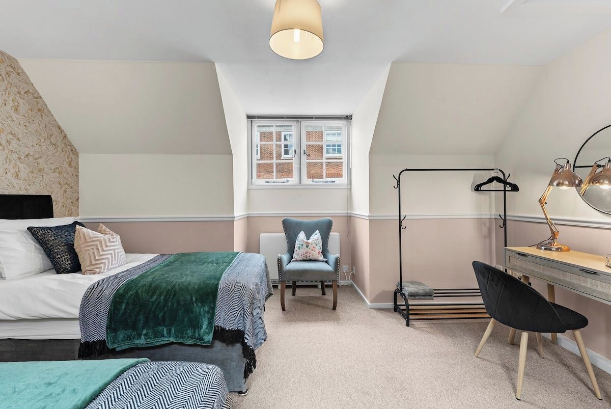 A bedroom with a bed, two chairs, a desk, a lamp, and a window.