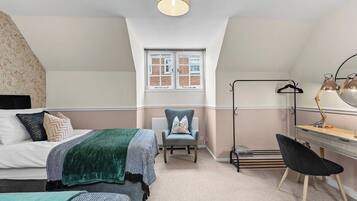 A bedroom with a bed, two chairs, a desk, a lamp, and a window.