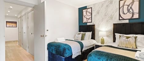 A hotel room with two beds, a marble wall, abstract art, and a wooden floor.