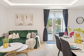 A modern living room with a green sofa, a round coffee table, and a dining area with a table set for two. - Comfortable London Retreat - Sleeps 6 (London)