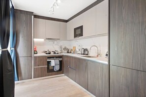 A modern kitchen with wood cabinetry, a marble countertop, and a built-in oven. - Comfortable London Retreat - Sleeps 6 (London)