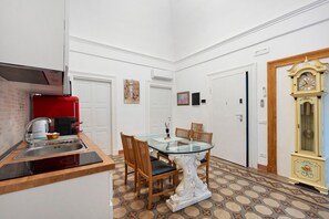 Cocina compacta con un electrodoméstico rojo, una mesa de comedor con sillas y un reloj decorativo.