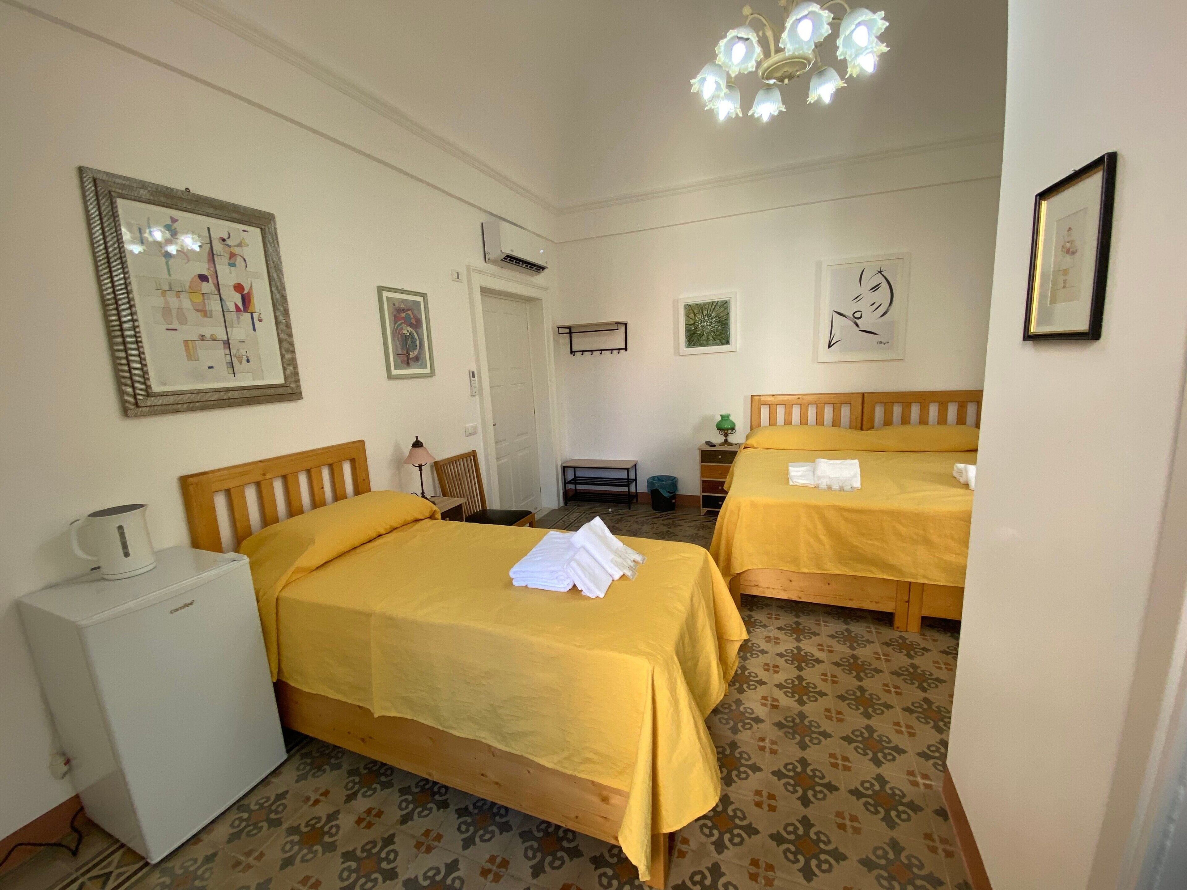 Ein Hotelzimmer mit zwei Betten, einem kleinen Schreibtisch, einem Kühlschrank und einem gestreiften Boden.