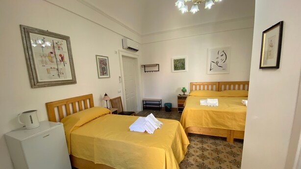 A hotel room with two beds, a small desk, a refrigerator, and a patterned floor. - Apartment 'Touristhouse Monopoli 10' with Balcony, Wi-Fi and Air Conditioning (Monopoli)