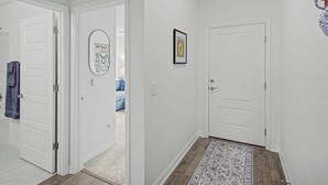 A hallway with white walls, a patterned rug, and a door leading to a room. - New Villa Beautifully Furnished Eastport Golf Cart Included (Sumterville)